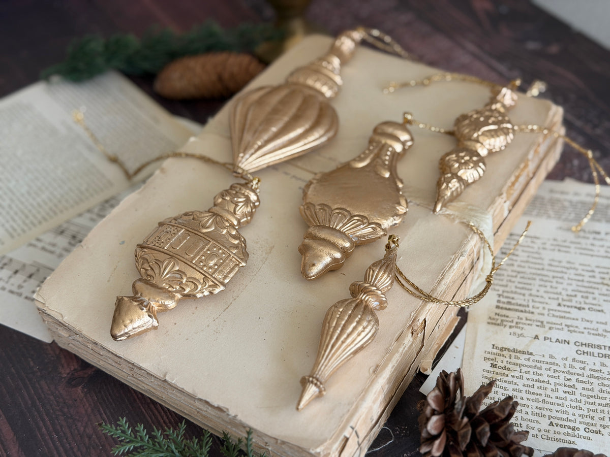 Five gold ornaments made with I.O.D. Baubles Mould (2026 Limited Release) displayed on a book.