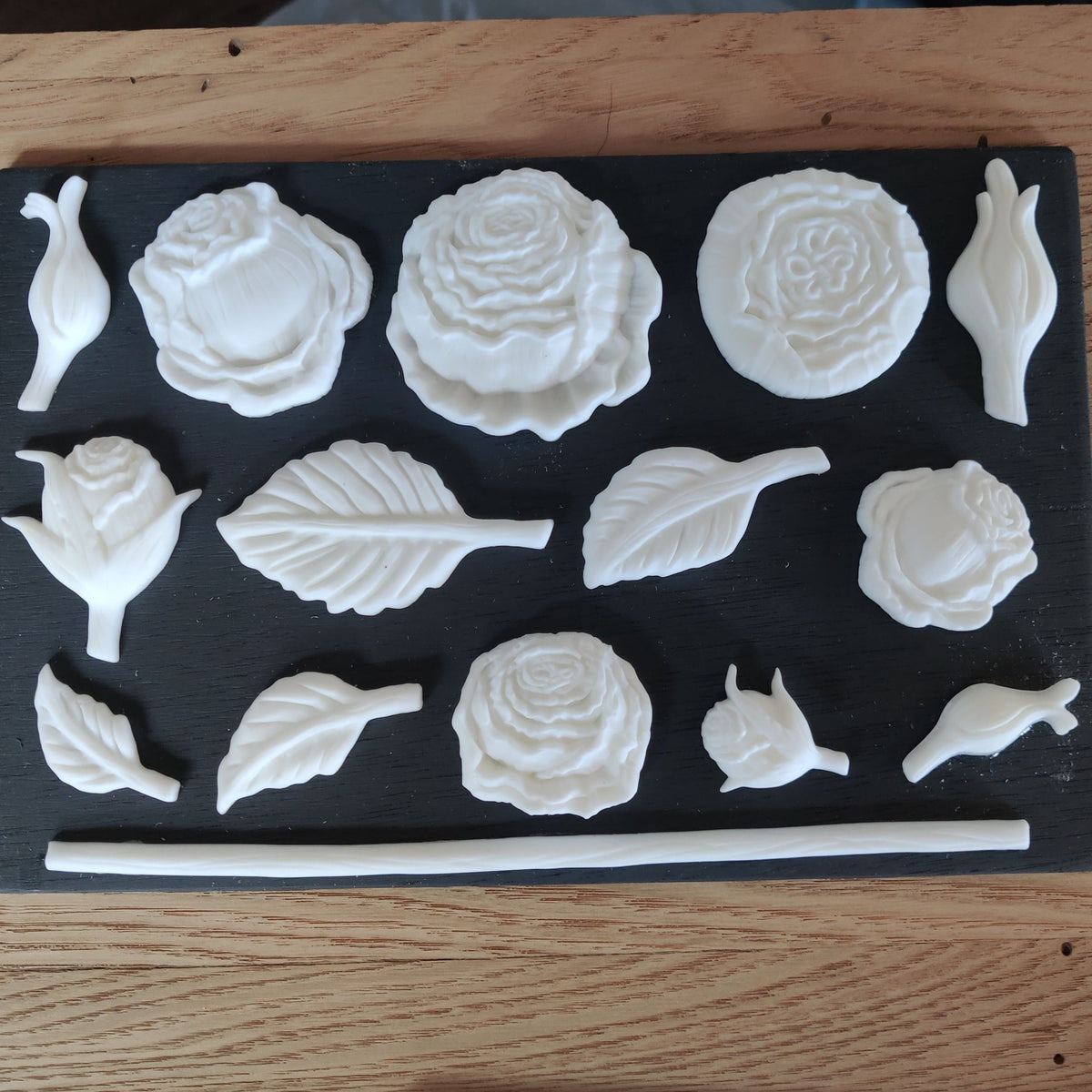 White rose, leaf, and bud shapes cast with Amazing Casting Resin (White) by Notions on a black background.