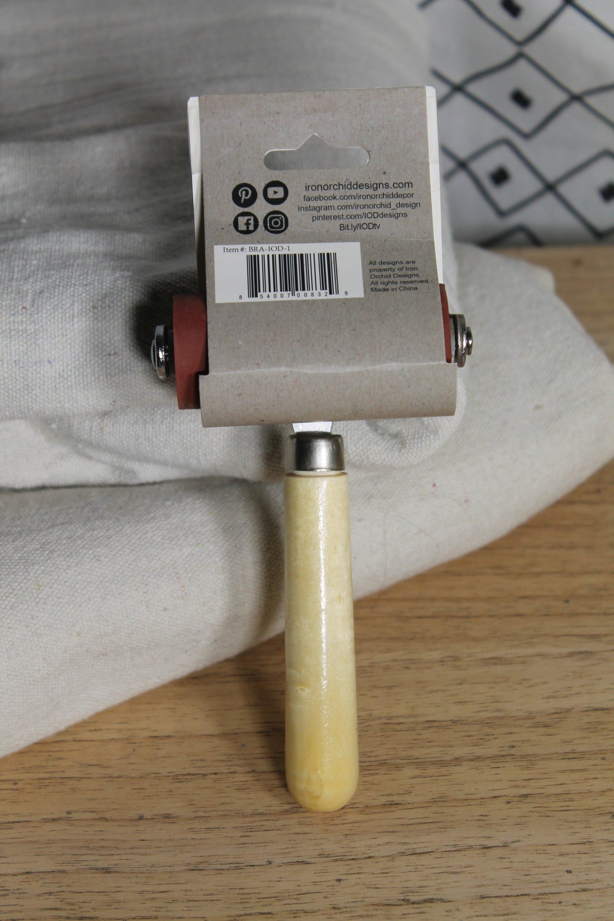I.O.D. Art Brayer with handle and tag shown on white cloth over wood.