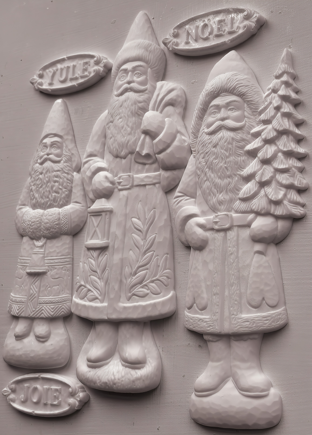 Three white Santas by I.O.D. Belsnickel Mould, each holding a YULE, NOEL, or JOIE sign; 2026 limited release.