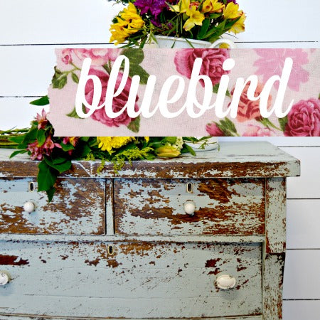 Distressed blue dresser with white knobs, floral bouquet, “Bluebird” pink fabric, painted in Old Fashioned Milk Paint.