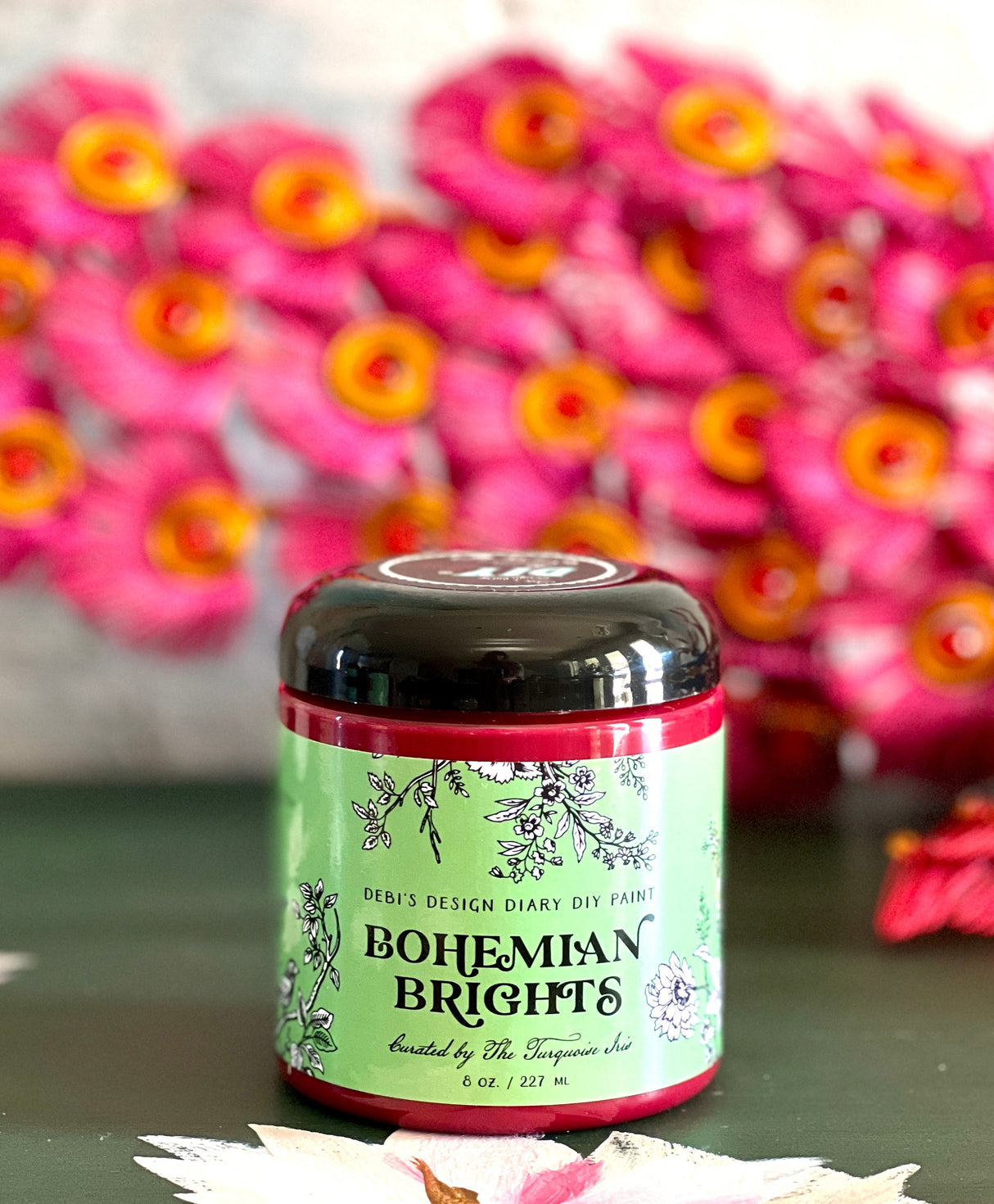 Bohemian Brights by DIY Paint Co. jar on green surface with pink artificial flowers in background.