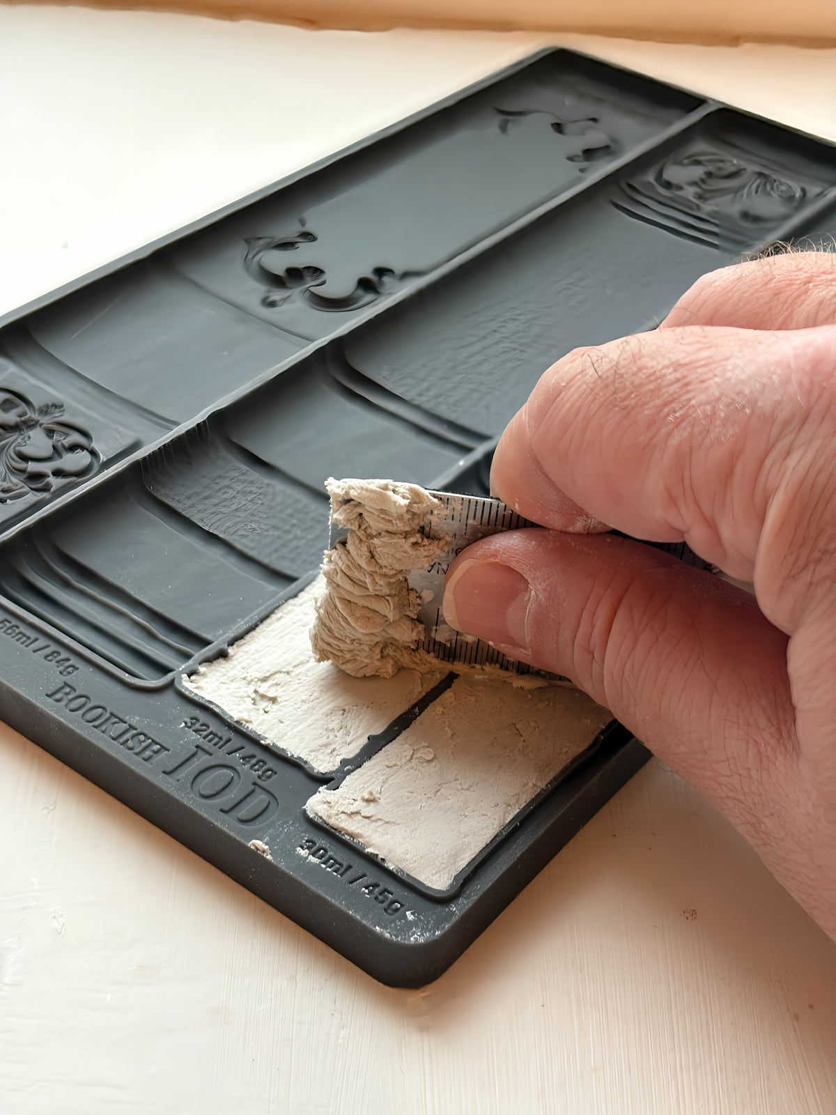 Hand applying white plaster into I.O.D. Bookish Mould on silicone, creating faux vintage book spine decor.