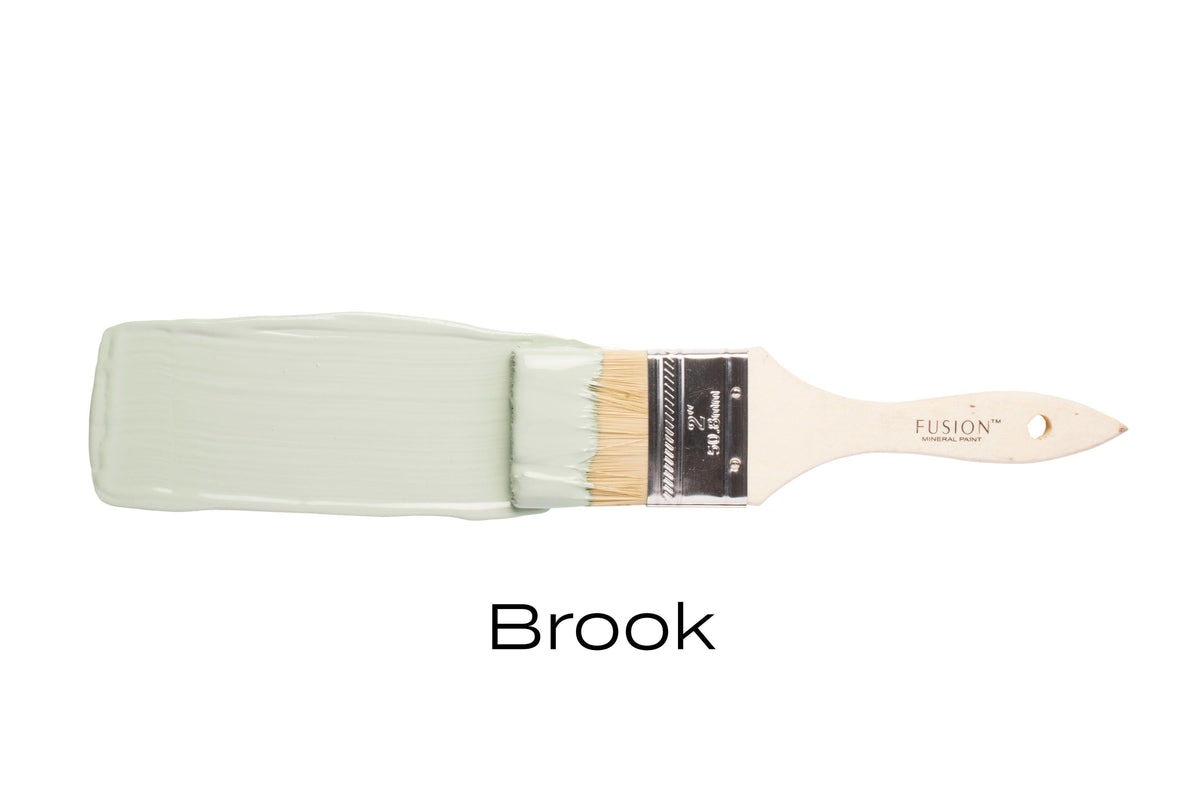 Paintbrush with Fusion Mineral Paint’s Brook, a vibrant blue-green shade, on a white background.
