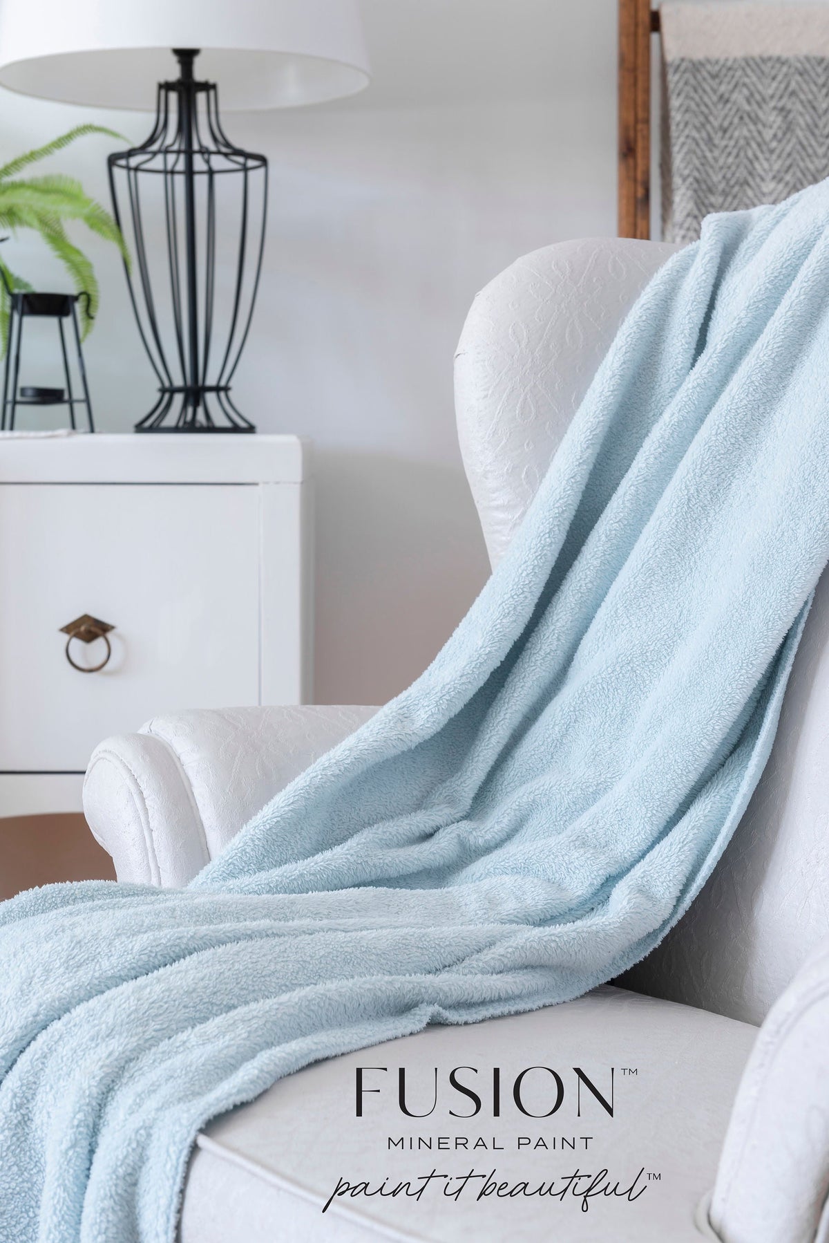 White chair with blue throw, set against Cashmere by Fusion Mineral Paint walls, beside a lamp and plant.
