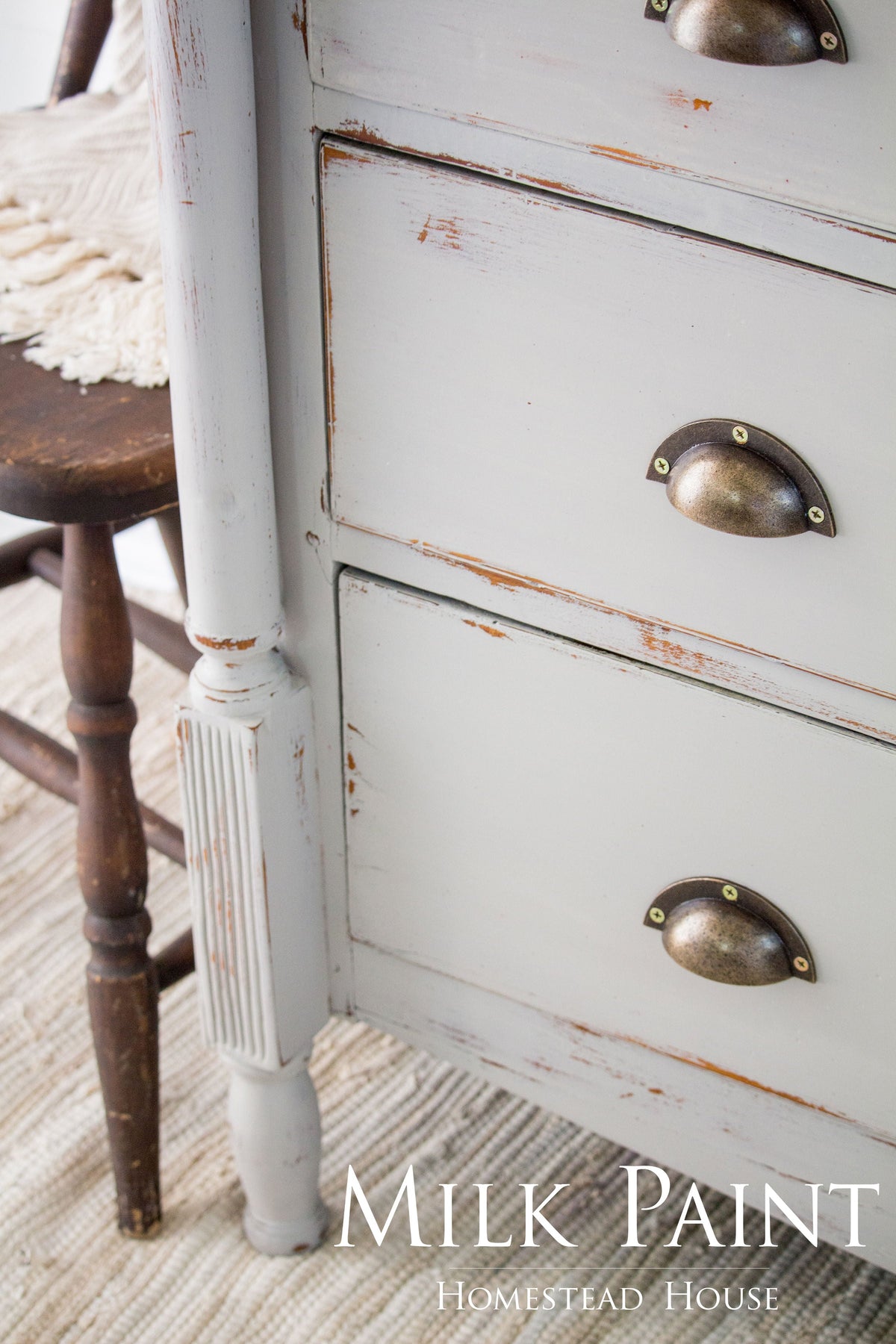White dresser with metal cup handles, finished in Homestead House Cathedral Taupe Milk Paint, next to a chair.