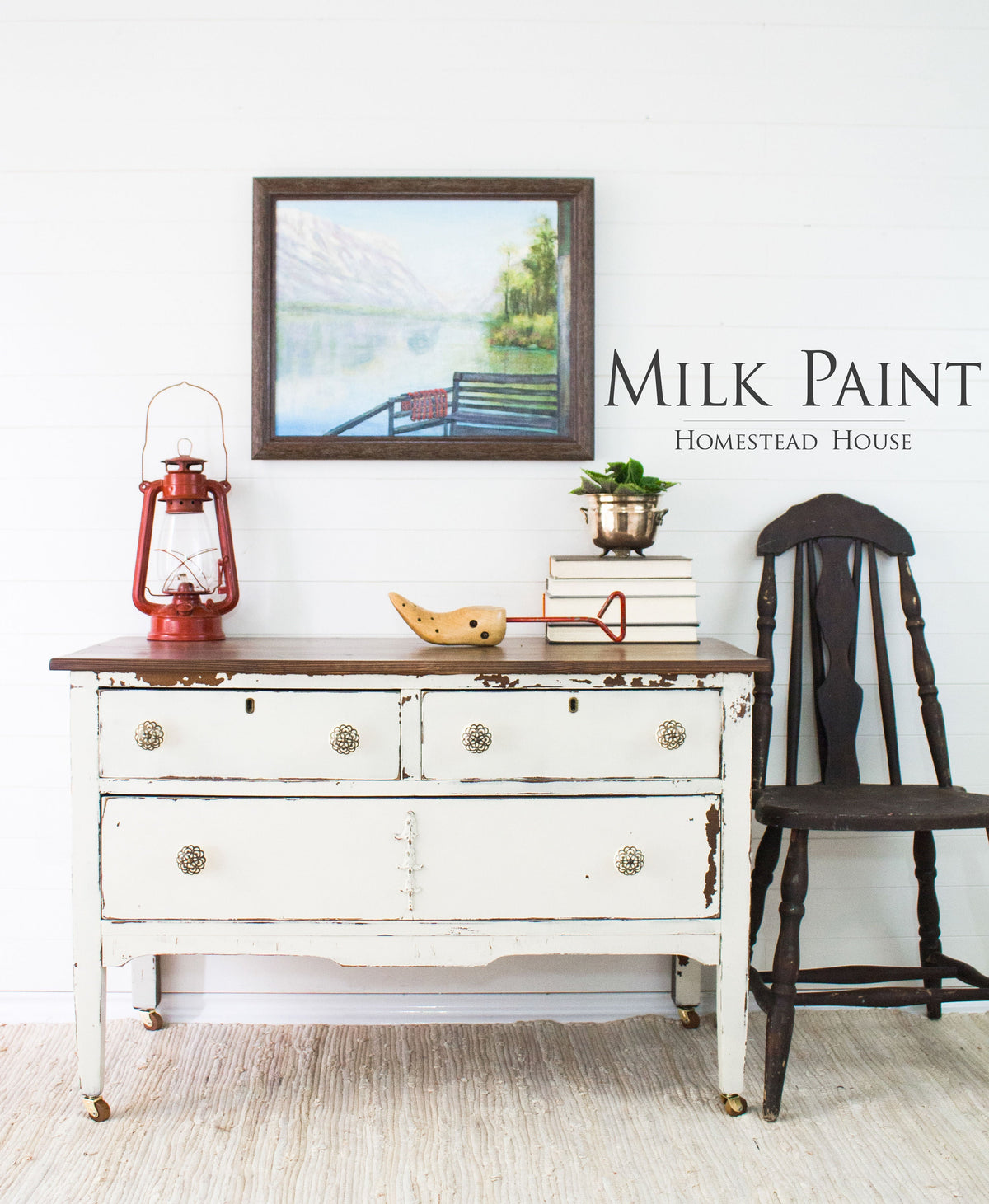 White distressed dresser painted with Champlain Milk Paint by Homestead House, styled with books, lantern, and wall art.