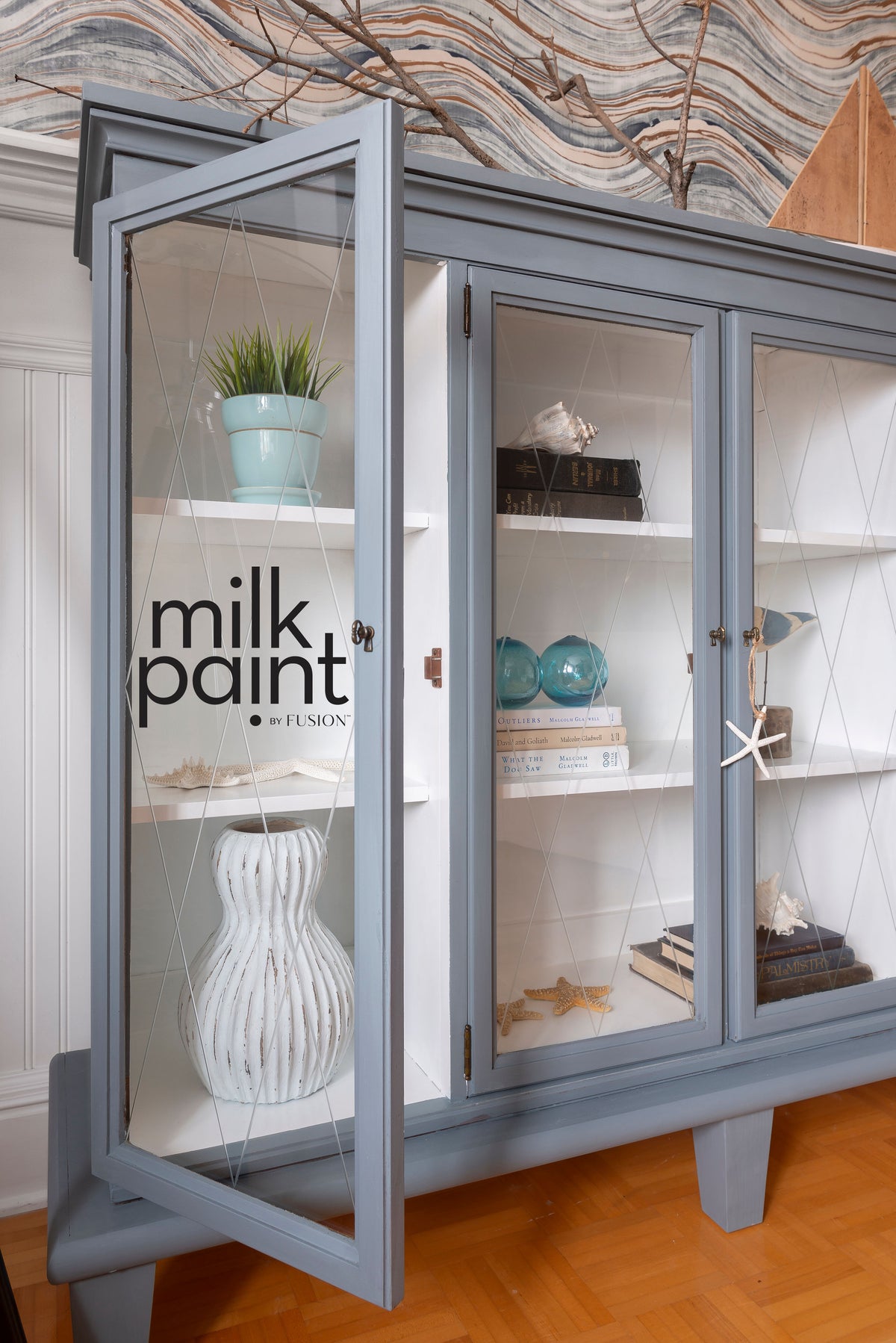 Display cabinet painted Coastal Blue by Fusion Mineral Paint, with glass doors showing books and decor inside.