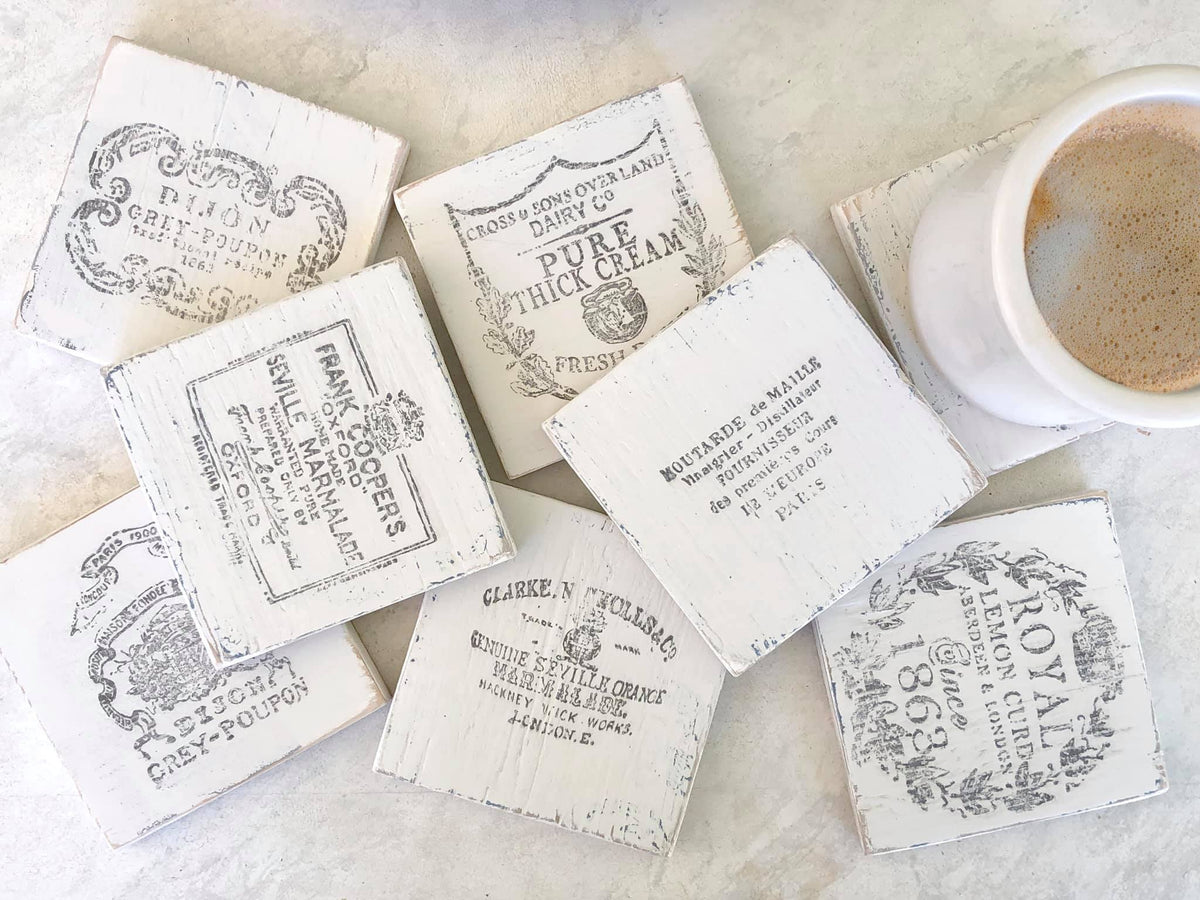 Seven vintage I.O.D. Crockery Stamp coasters by Iron Orchid Designs shown next to a white coffee cup.