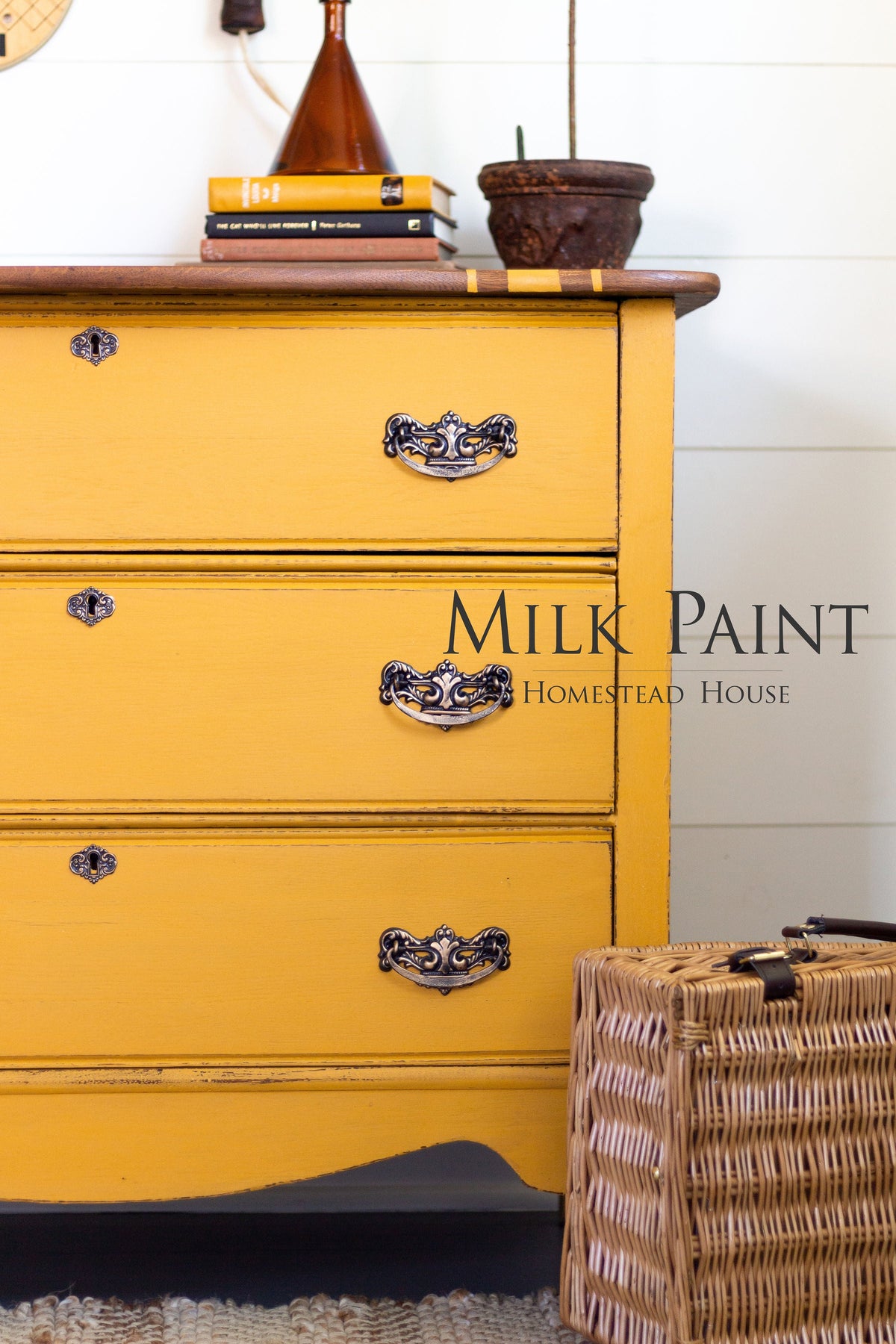 Yellow dresser with ornate handles, books, lamp, plant; wicker basket; text: Garden Seed Milk Paint by Homestead House.