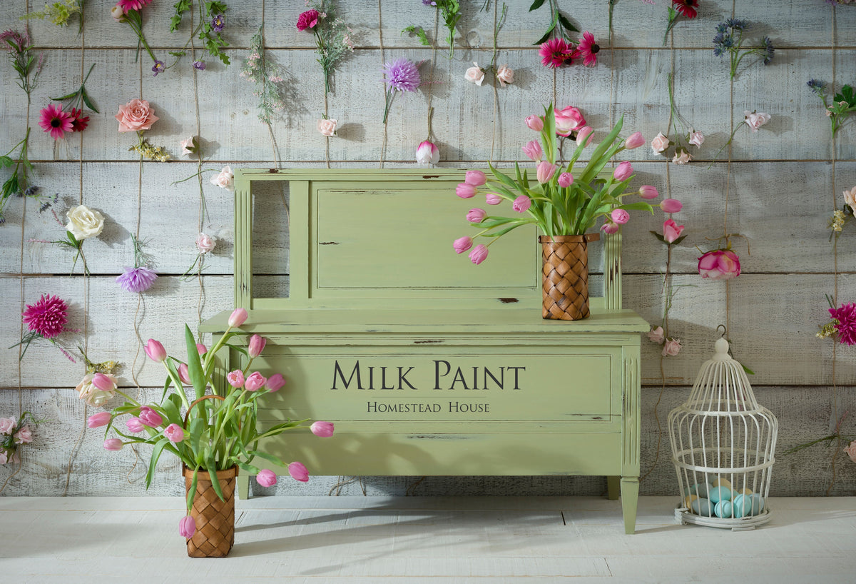 Green bench painted with Gatineau Milk Paint by Homestead House, with pink tulips and a birdcage on the right.