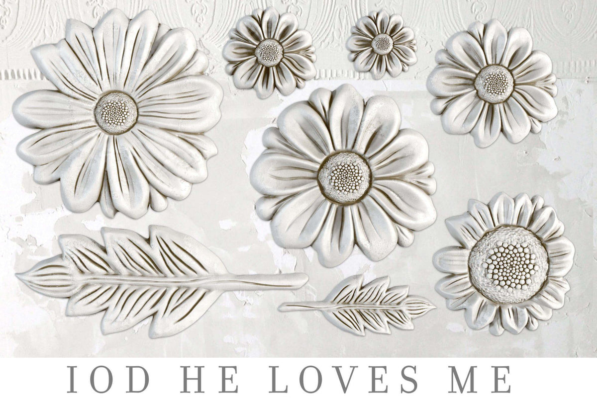 Seven white floral and leaf accents made with I.O.D. He Loves Me Mould displayed on a textured surface.