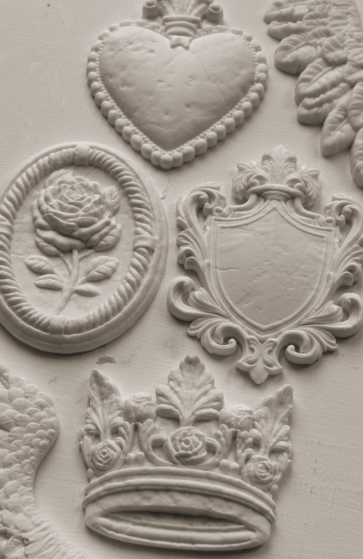 I.O.D. Heraldry Mould white reliefs with hearts, roses, shields, and crowns in decorative designs.