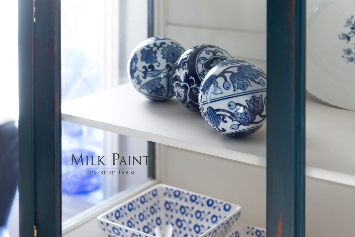 Three blue and white porcelain balls inspired by Homestead Houseās Homestead Blue Milk Paint near a patterned dish.