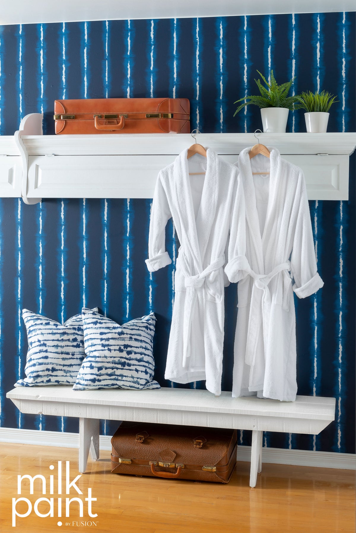Two Hotel Robe Milk Paint robes by Fusion Mineral Paint hanging above a bench; shelf above holds luggage and plants.
