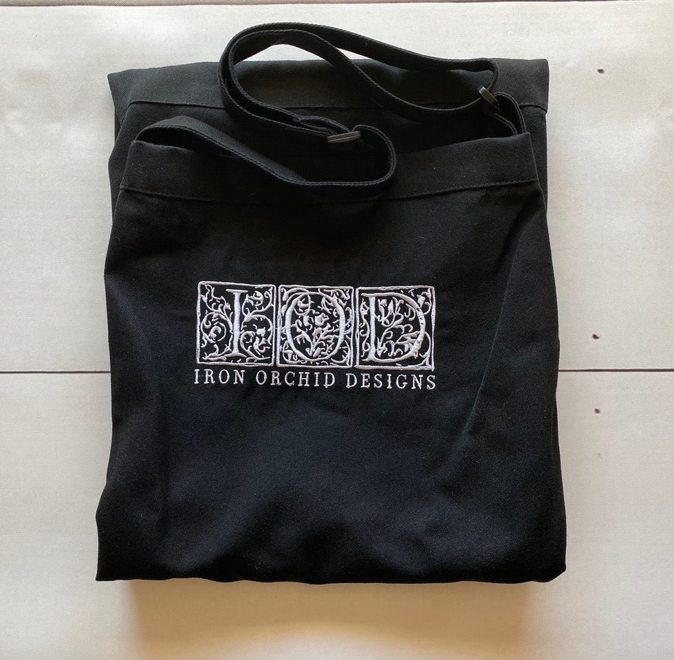 Black I.O.D. apron with ornate white lettering by Iron Orchid Designs on a light background.