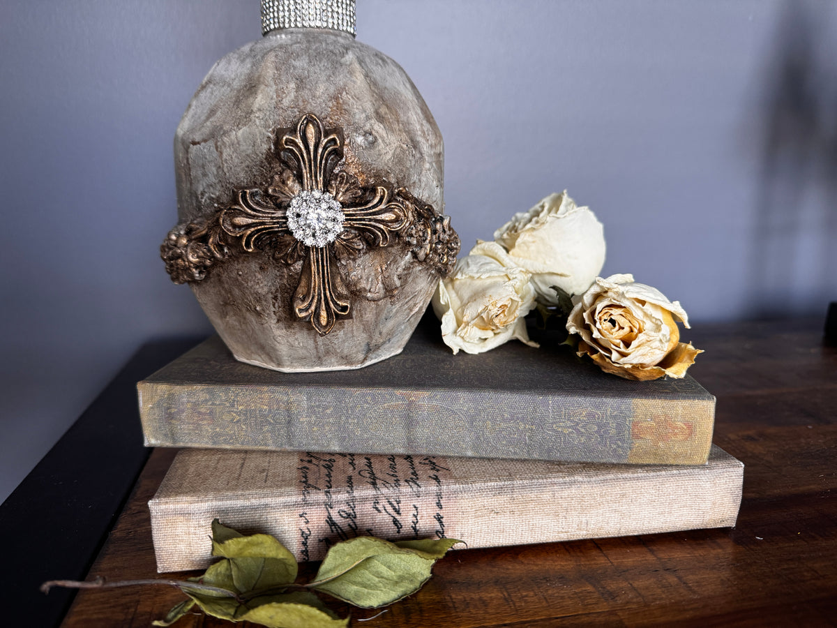 Les Croix Mould decorative bottle by I.O.D. displayed on vintage books with dried roses and green leaves.