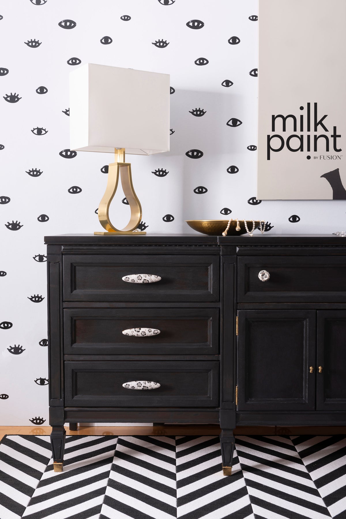 Black sideboard with drawers, gold lamp, and bowl on top; chevron rug below; wall in Little Black Dress paint.