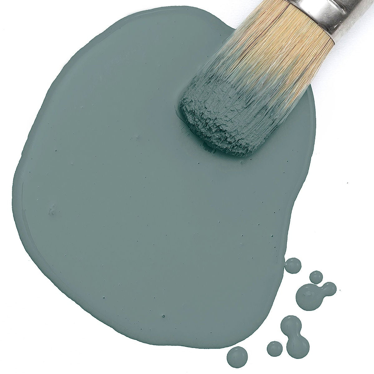 Brush with light bristles in wet Monterey Milk Paint by Fusion Mineral Paint, with small paint splatters nearby.
