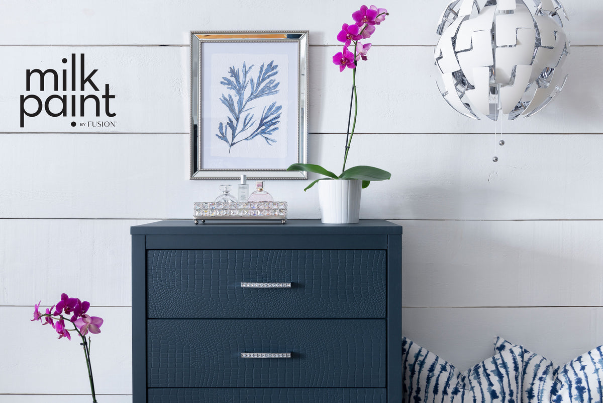 Dark blue dresser with orchids; “Night Swim Milk Paint by Fusion Mineral Paint” text on white shiplap wall.