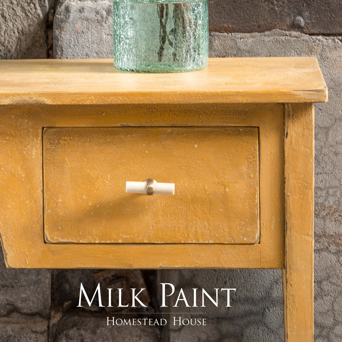 Yellow wooden table painted in Prairie Sunset Milk Paint with drawer, glass vase, and visible Homestead House branding.