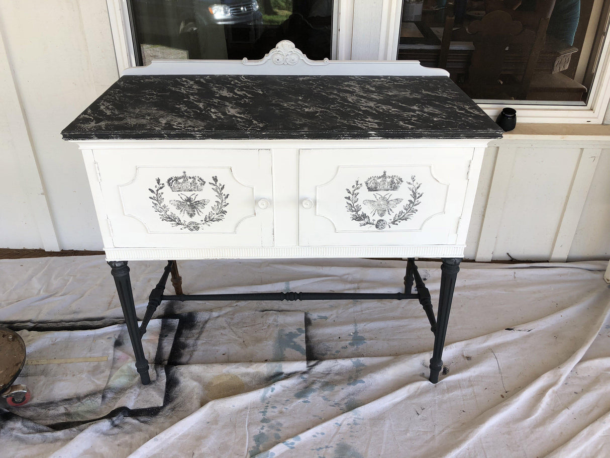 White cabinet with black legs, marble top, and I.O.D. Queen Bee Stamp detail.