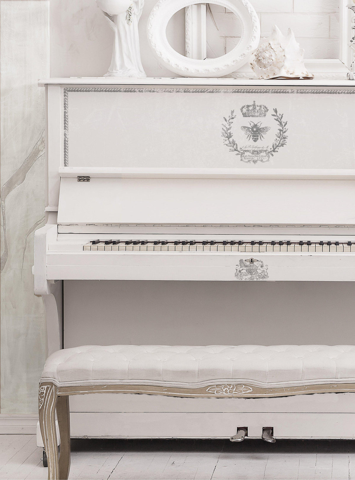 White upright piano with I.O.D. Queen Bee Stamp motifs, matching bench, and white decor on top.