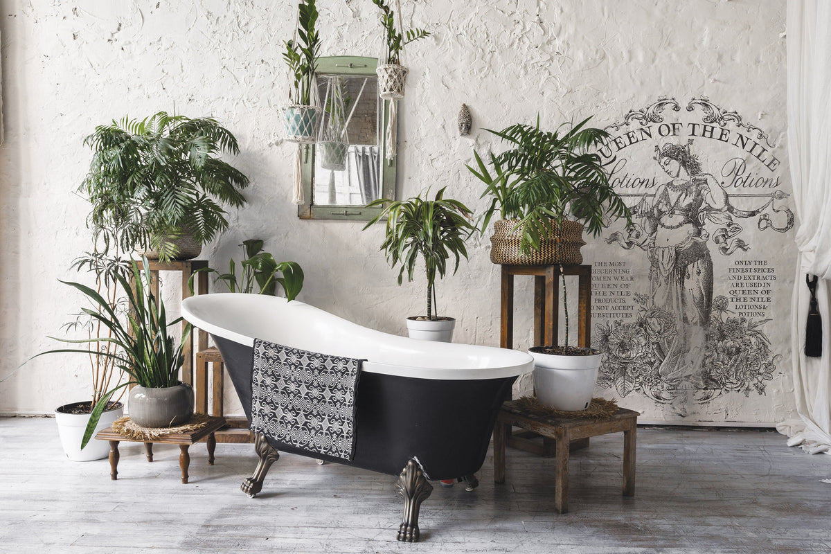 Black clawfoot tub in rustic room with Queen of the Nile Paint Inlay by I.O.D., plants, and a towel nearby.