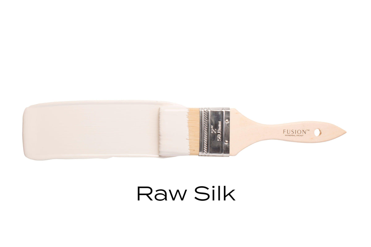 Brush with Fusion Mineral Paint Raw Silk, warm white acrylic paint, displayed on a plain white background.
