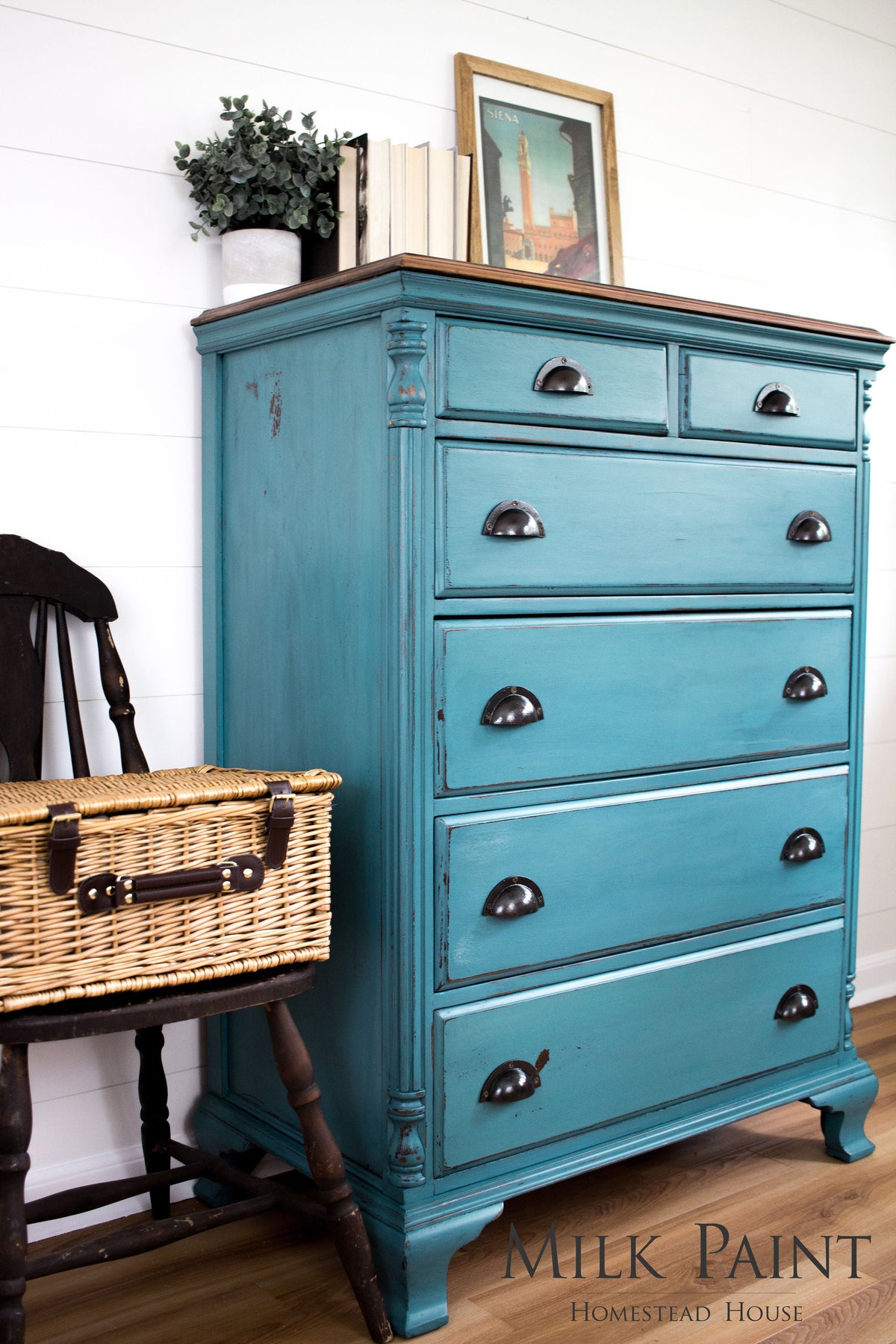 Teal dresser painted with Homestead House Renfrew Blue Milk Paint next to a dark chair in a bright room.