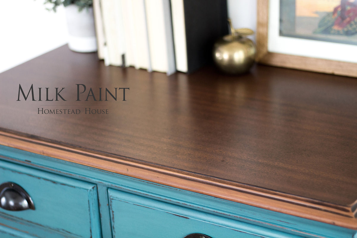 Teal dresser in Homestead House Renfrew Blue Milk Paint with dark wood top, books, brass apple, and framed art.