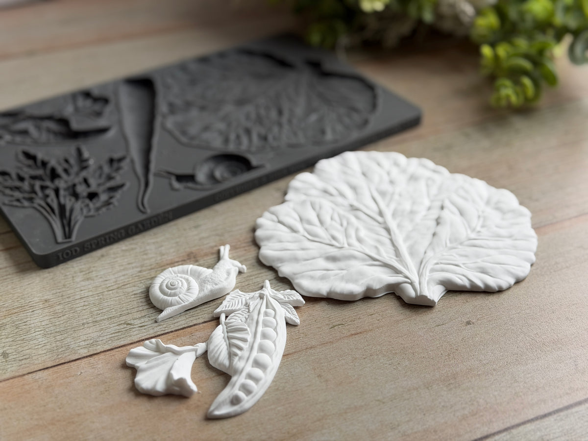 Spring Garden Mould by IOD featuring leaf, snail, flower, and pea pod designs arranged on wood.
