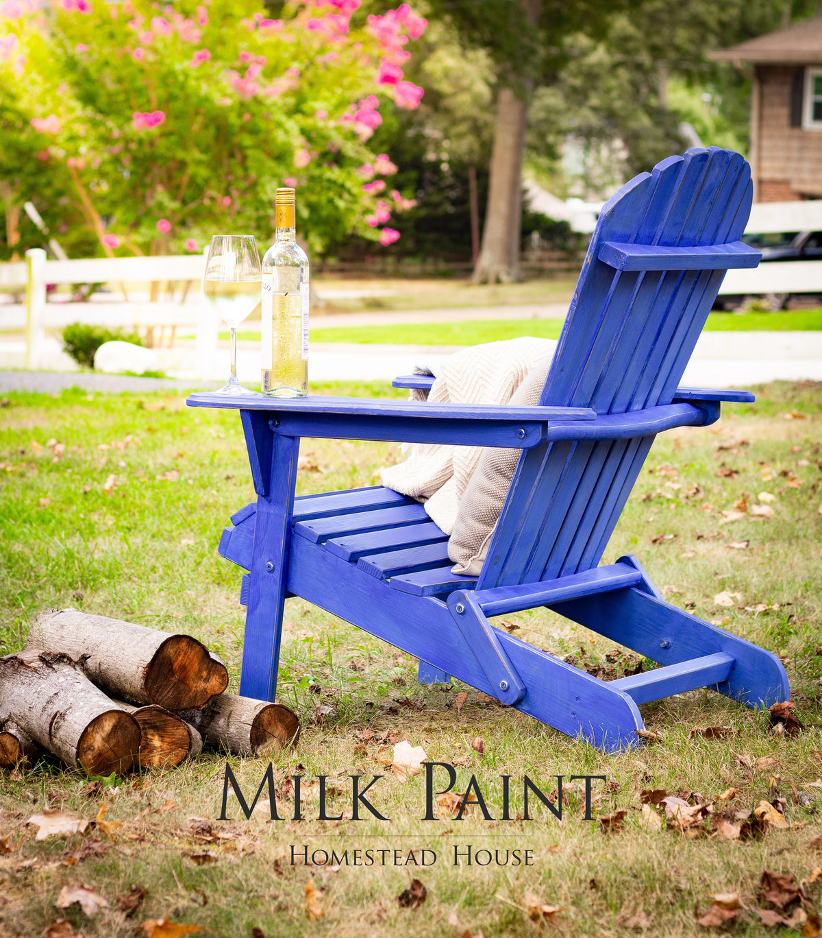 Homestead House Adirondack chair in St-Laurent Blue Milk Paint with wine and firewood on grass.