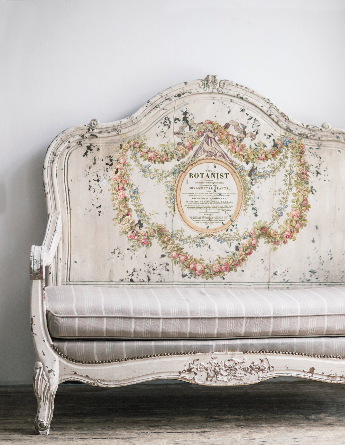 Antique white bench with I.O.D. Botanist Transfer, floral garland, distressed wood, botanical back, striped cushion.