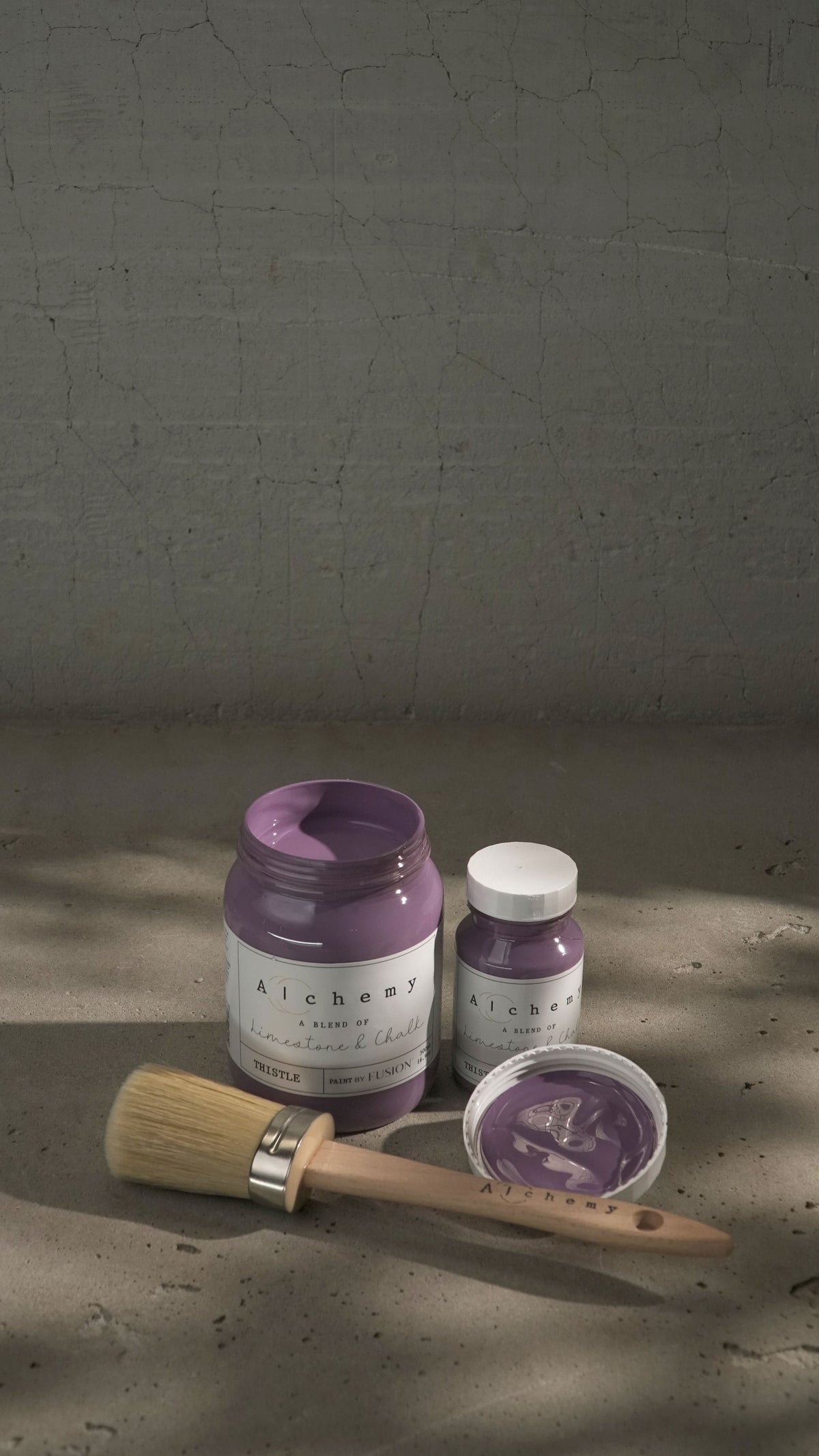 Three jars of Thistle Alchemy Paint by Fusion Mineral Paint, one open, with a paintbrush nearby.