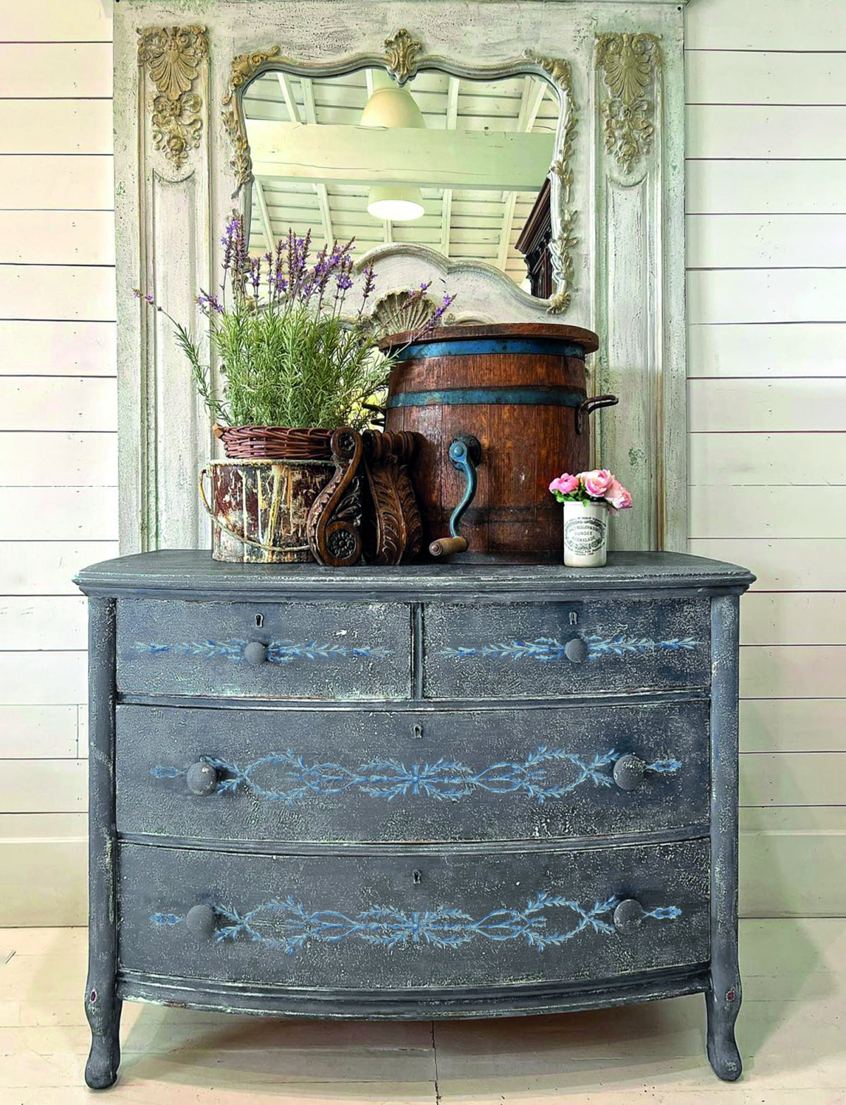 Blue vintage dresser with I.O.D. Trompe L’oeil Bleu Paint Inlay, topped with mirror, flowers, barrel, and decor.