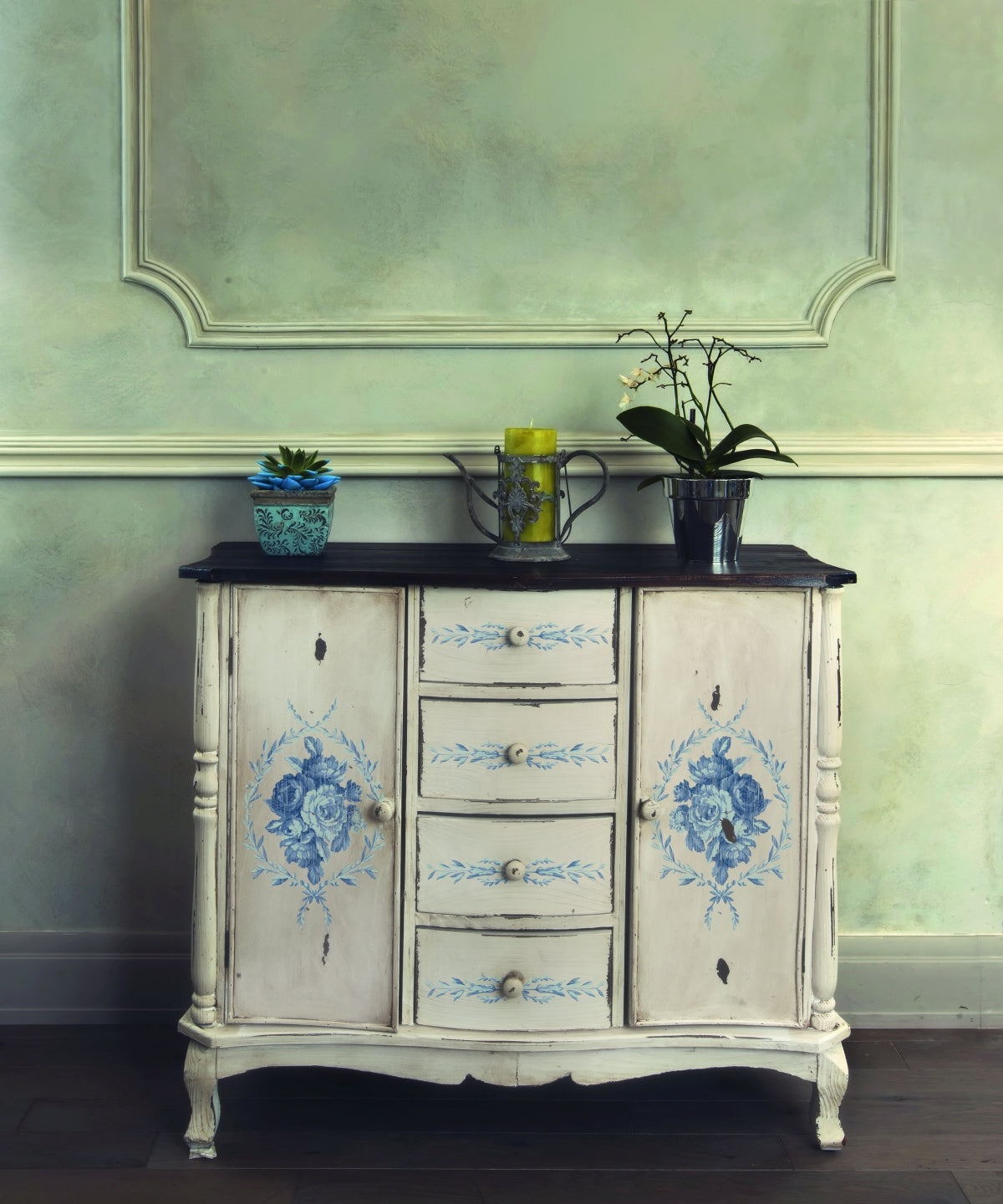 White cabinet with I.O.D. Trompe L’oeil Bleu Paint Inlay, topped with a potted plant and metal watering can.