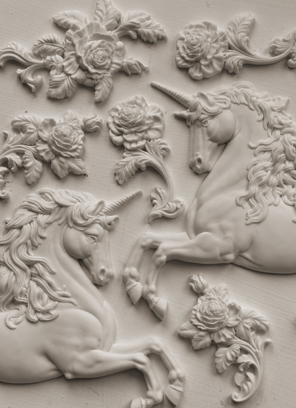 Two white-relief unicorns and flowers made with the Unicorns Mould by IOD on a flat surface.