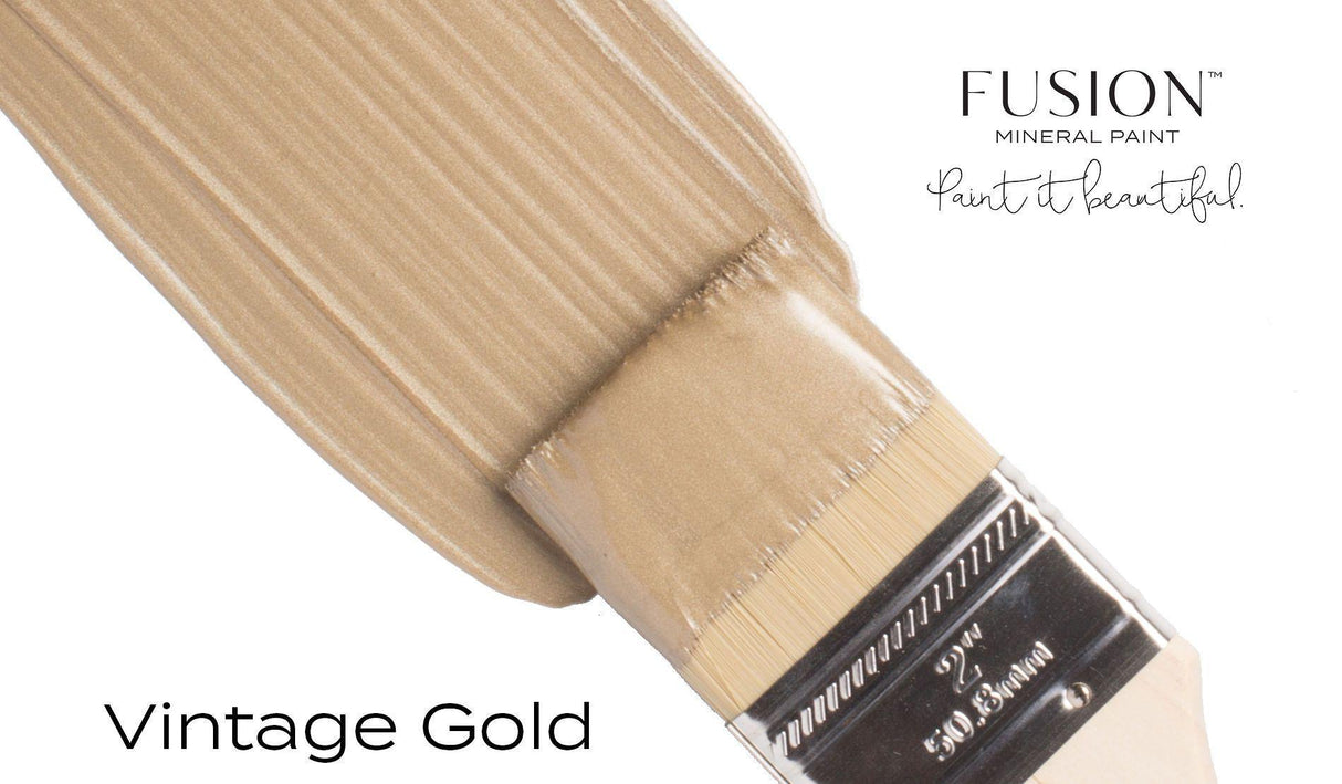 Brush applying Vintage Gold Metallic Fusion Mineral Paint with mica pigments onto a white surface.
