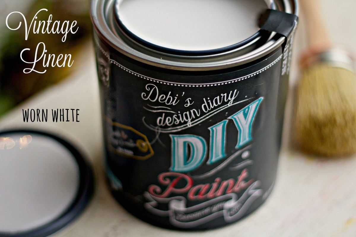 Open can of Vintage Linen DIY Paint by DIY Paint Co. with lid and brush placed nearby on a flat surface.