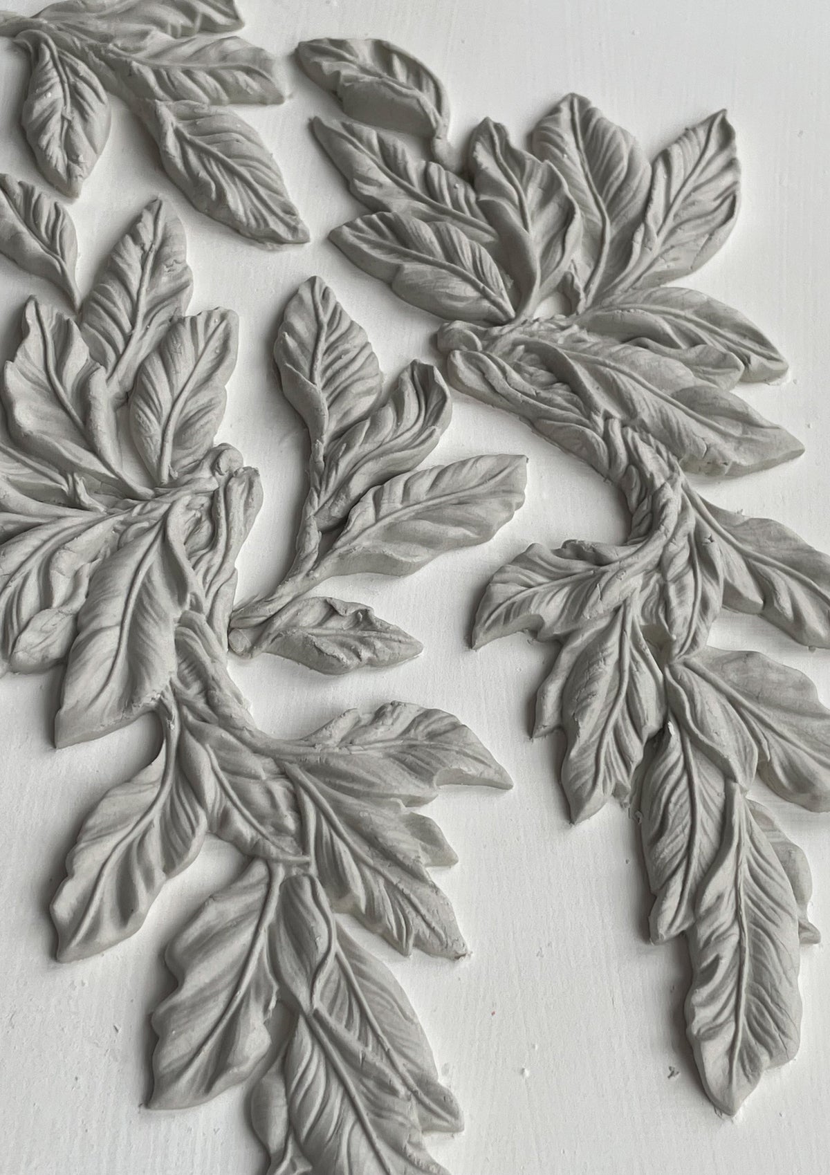 White clay leaves with detailed veins made with I.O.D. Viridis Mould by Iron Orchid Designs, arranged on white.