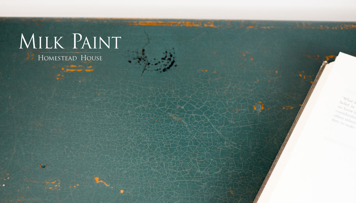 Distressed Waterloo Green Milk Paint surface by Homestead House with an open book positioned on the right side.