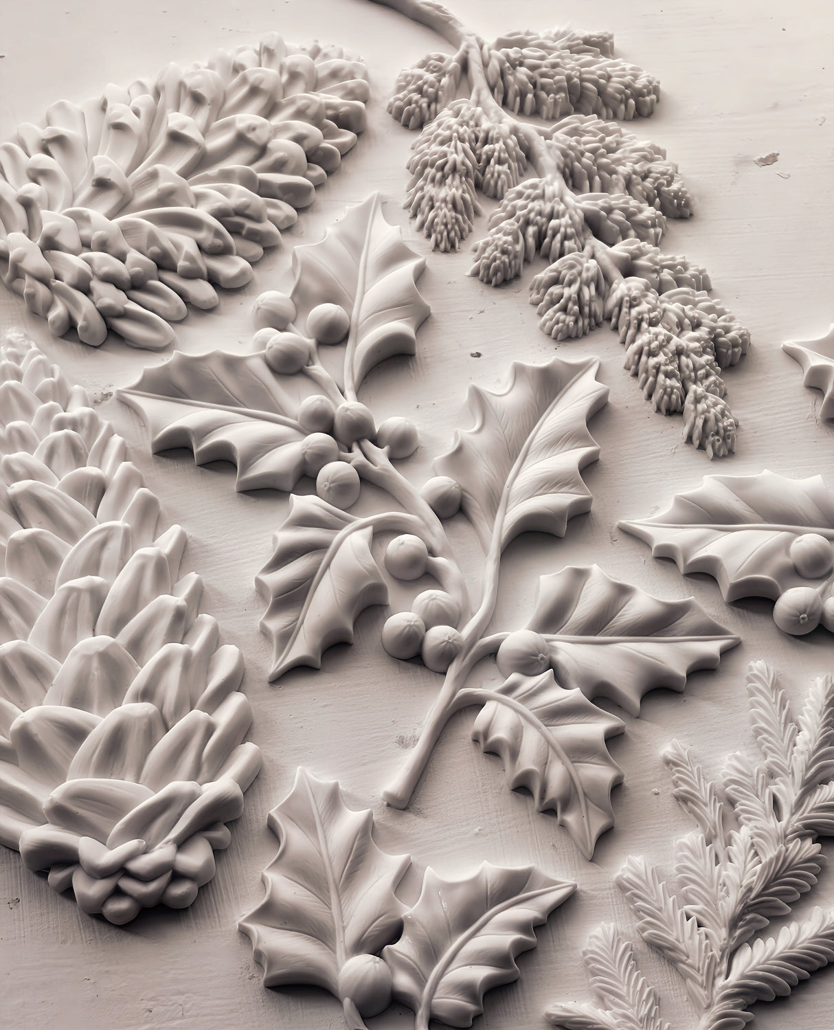 Pinecones and holly leaves crafted using I.O.D. Winter Forage Mould (2025 Limited Release) on white textured surface.