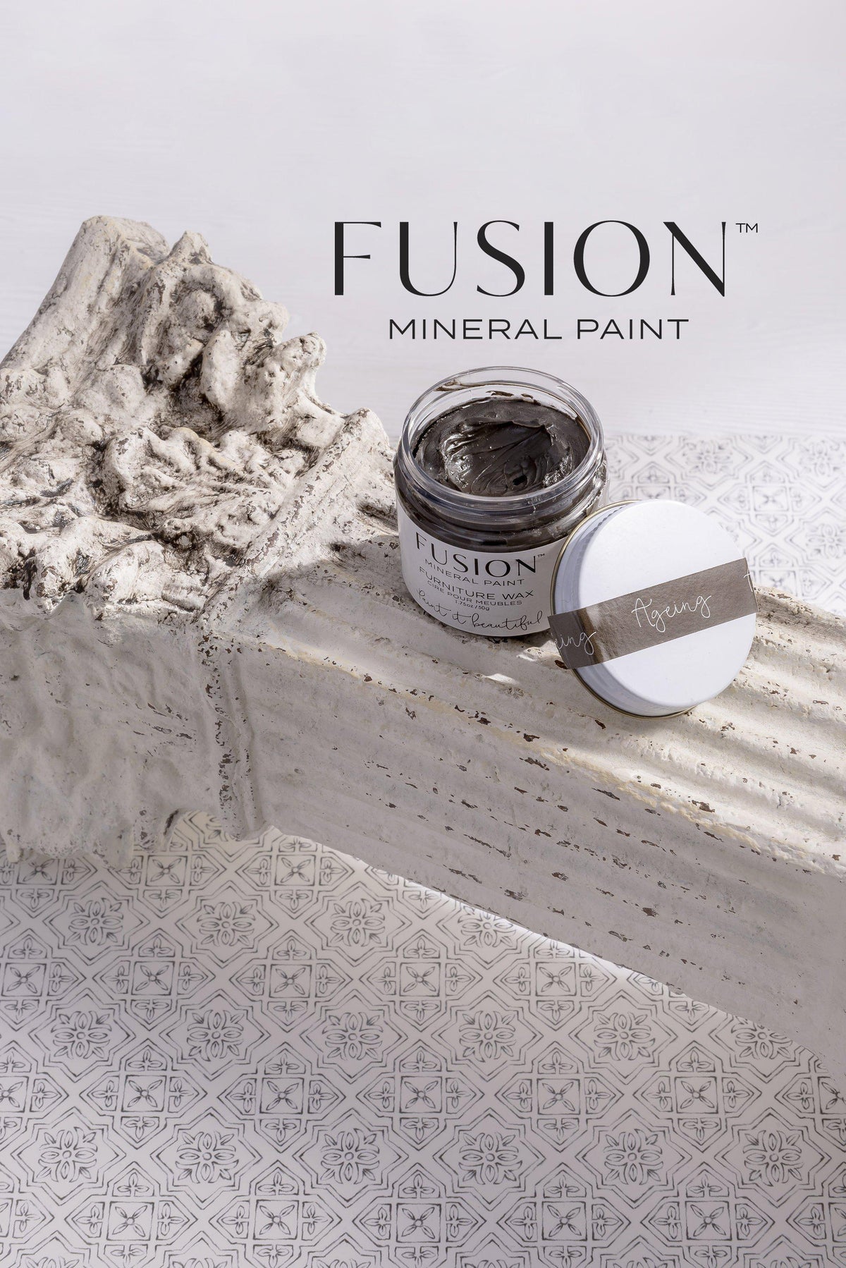 Open jar of Ageing Furniture Wax by Fusion Mineral Paint with lid beside it on a stone ledge.