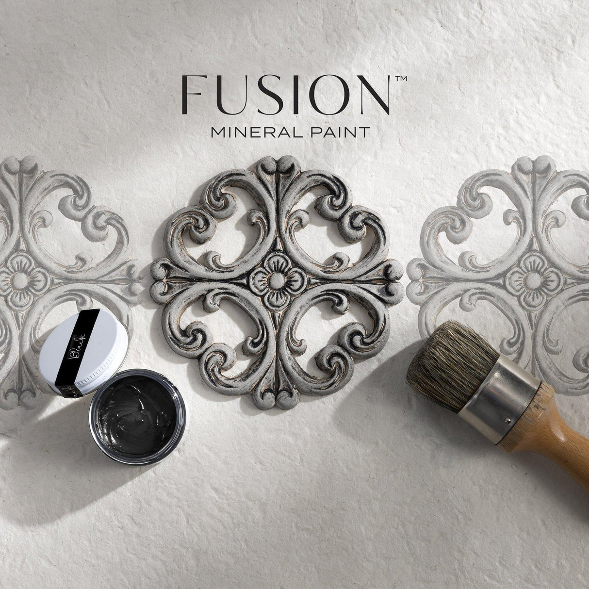 Round stencil, paintbrush, and Fusion Mineral Paint Black Furniture Wax with two stenciled designs on white surface.