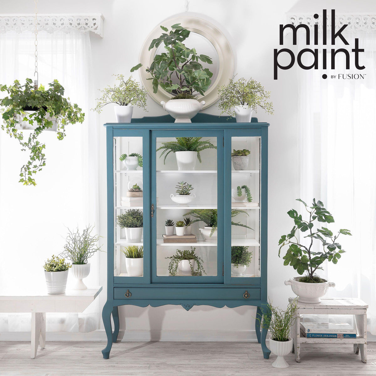 Blue cabinet with glass doors showcasing potted plants painted in Fusion Mineral Paint’s Terrarium Milk Paint.