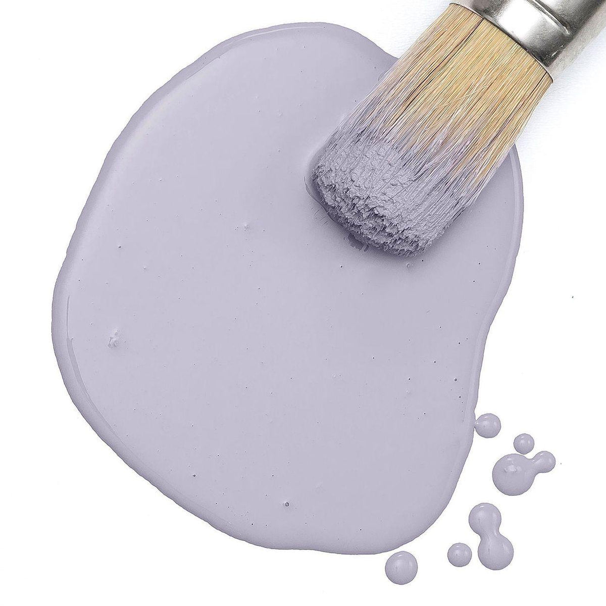 Paintbrush resting on spilled Wisteria Row Milk Paint by Fusion Mineral Paint with purple drops on white.