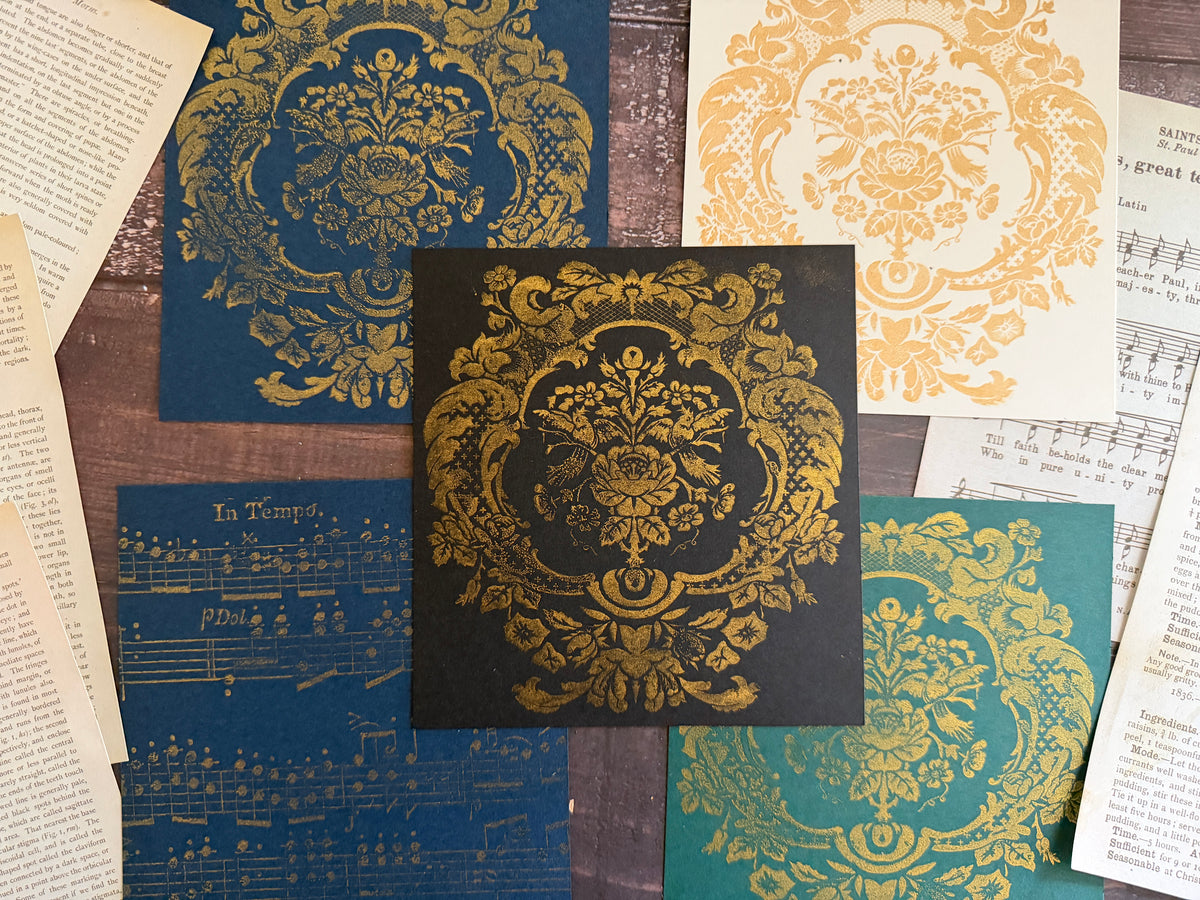 Five floral prints made with I.O.D. Metallic Ink Pads on colored paper, bordered by vintage book and music pages.