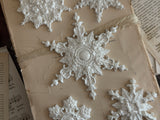 I.O.D. Snowflakes Mould (2026 Limited Release) white snowflake ornaments arranged on aged book paper with ribbon.