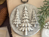 Gray I.O.D. Boughs of Holly ornament (2026 Limited Release) with three white pine trees and a pine cone design.